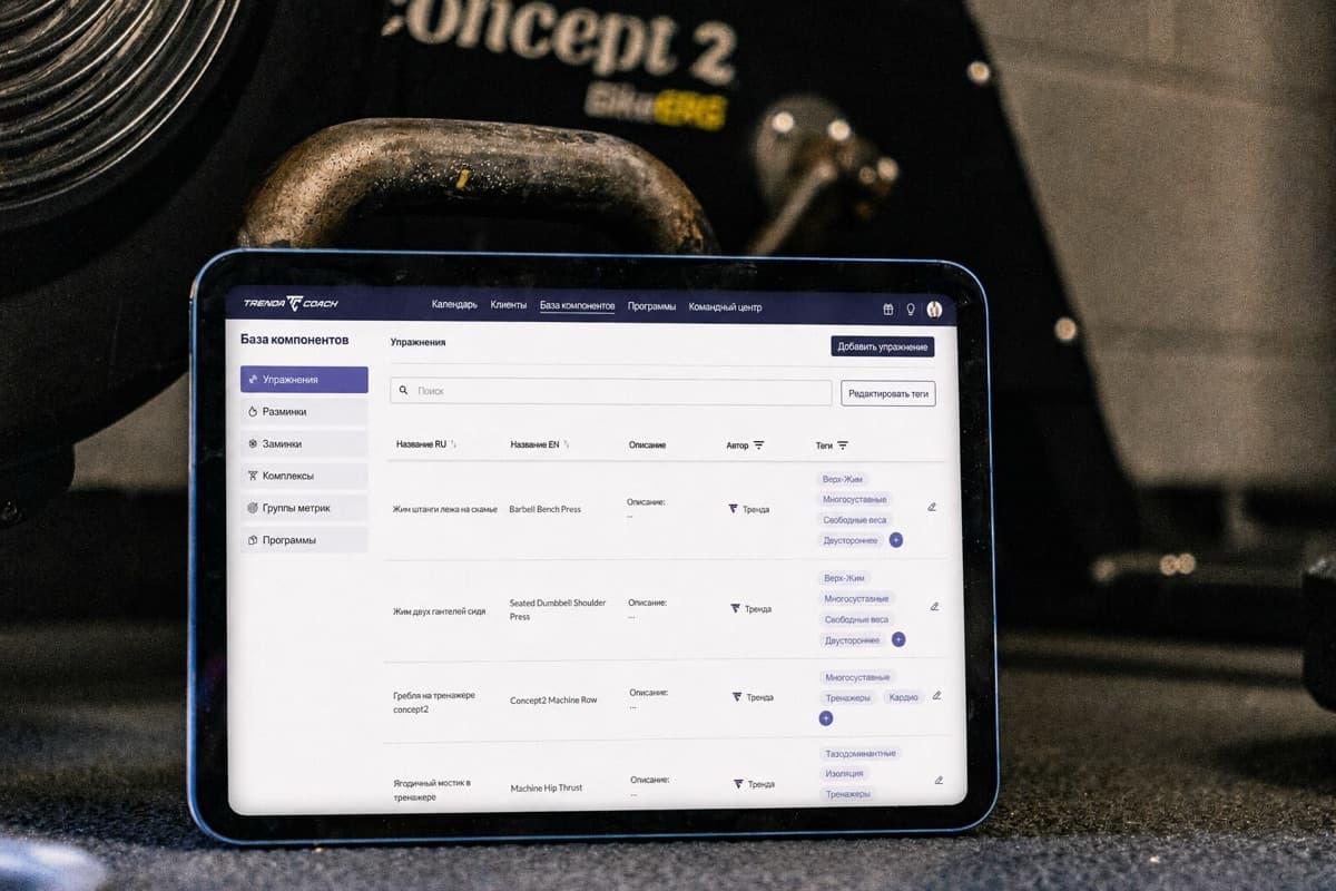 База упражнений Trenda Coach на экране планшета рядом с тренировочным оборудованием